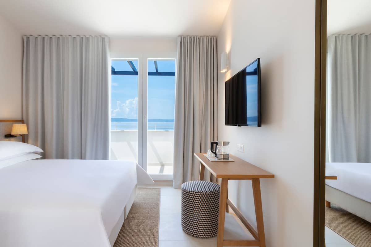 Habitación de hotel con cama, escritorio con cafetera, televisor y vista al mar por la ventana.