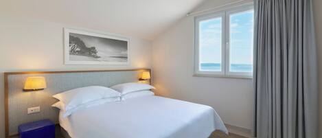 A hotel room with a bed, two bedside lamps, a nightstand, a framed picture on the wall, and a window with curtains.