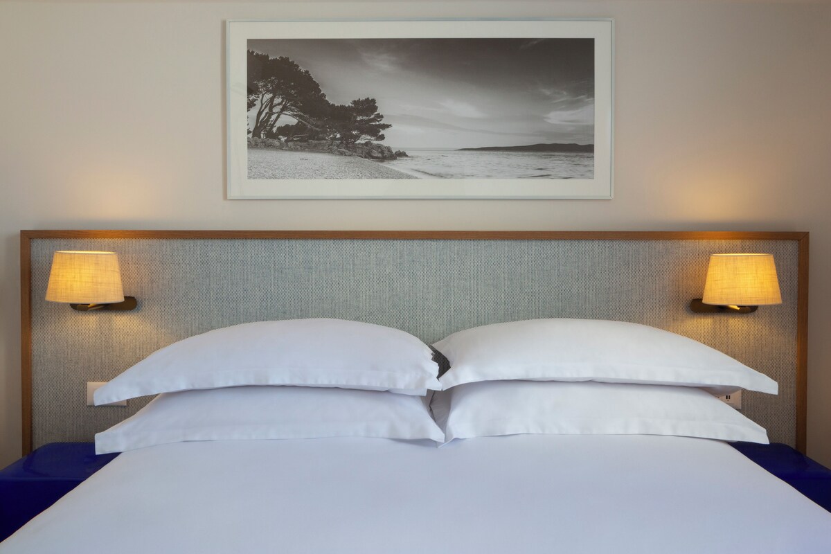 A neatly made bed with white linens and two pillows, flanked by two wall-mounted lamps.