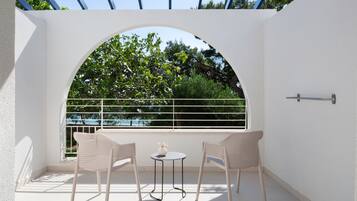 A balcony with two wicker chairs and a small table, a white railing, and a view of trees and a blue sky.