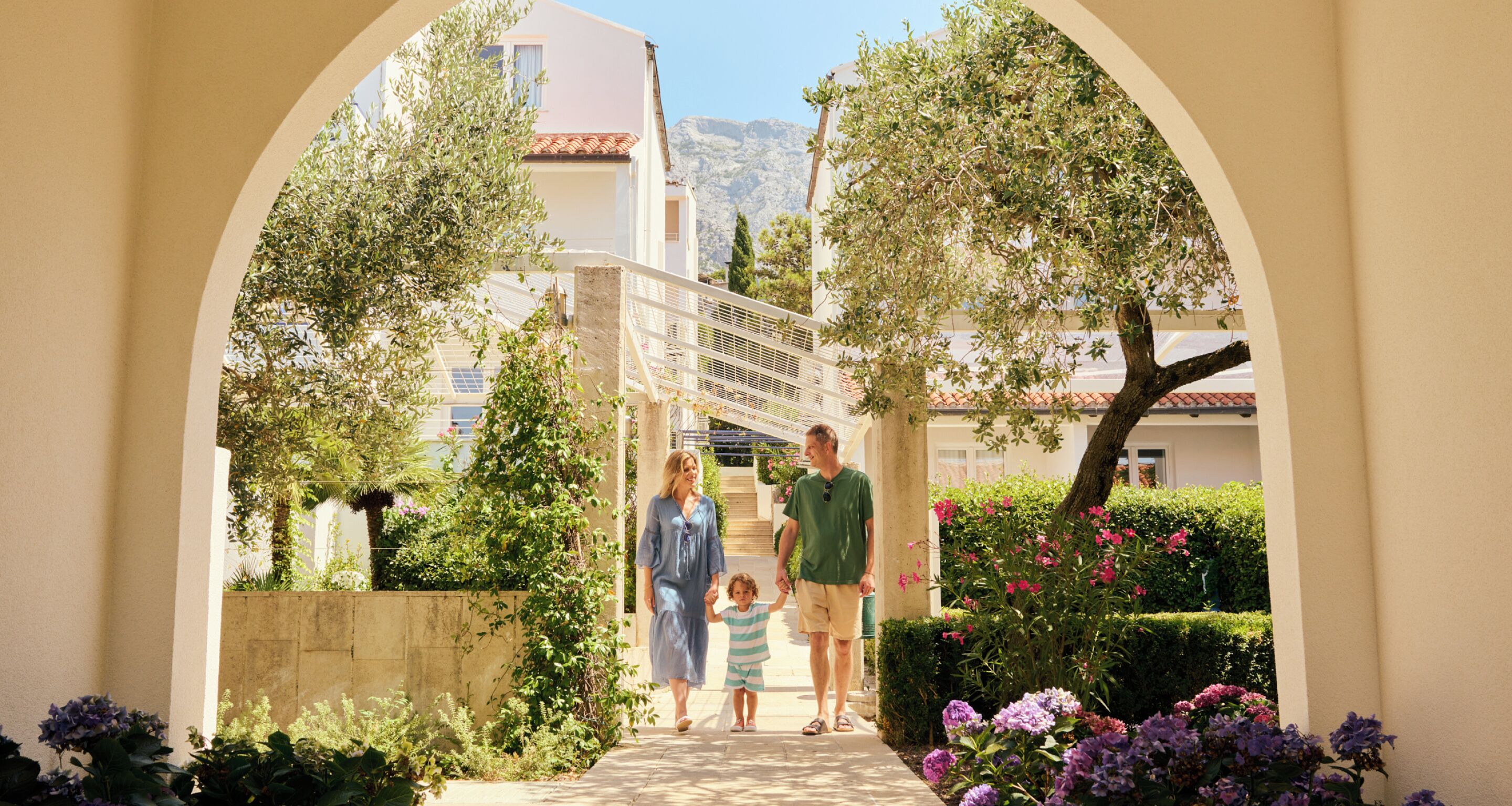 A pathway leading to a building with a covered walkway, surrounded by greenery and flowers.