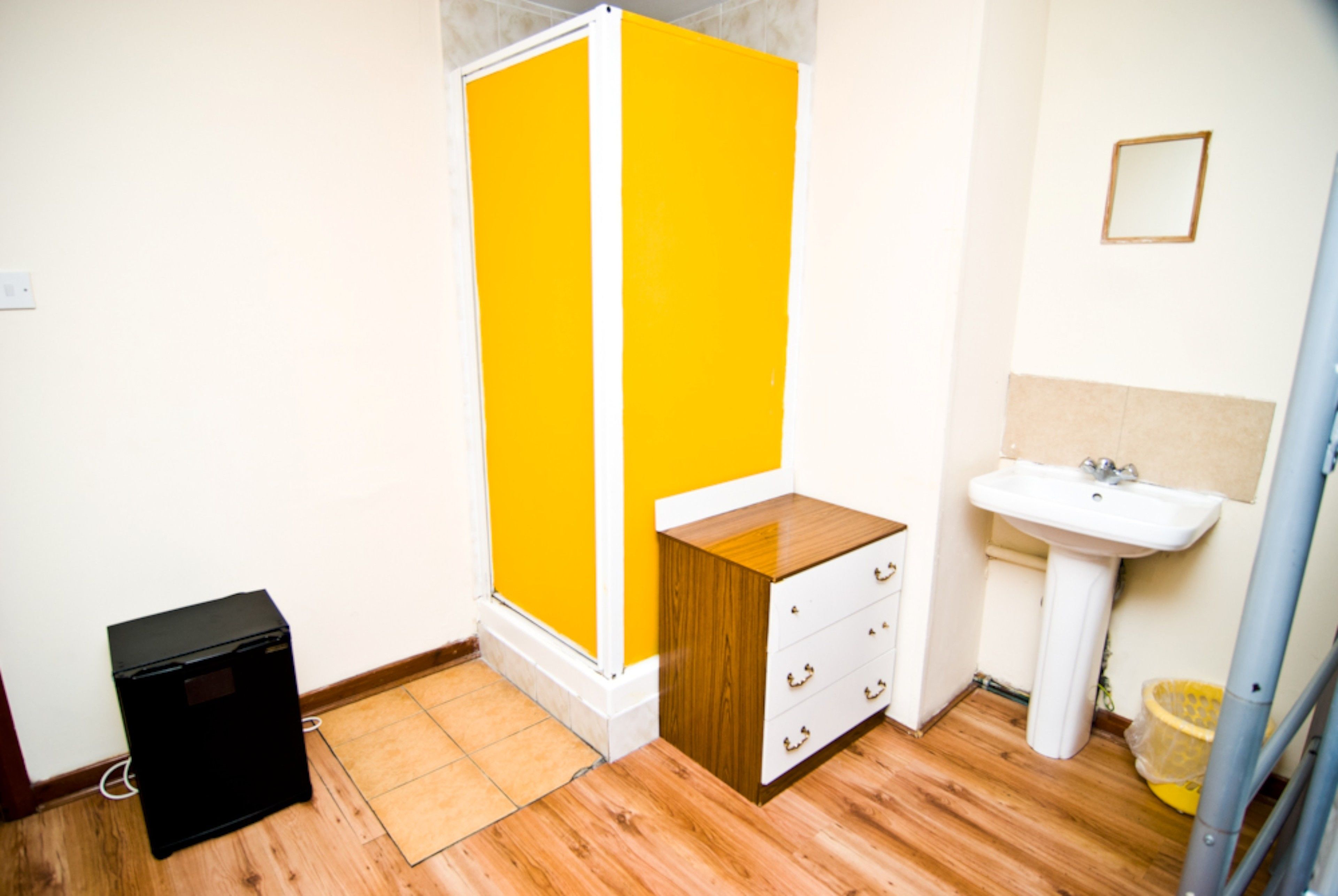 A bathroom with a yellow shower enclosure, a white sink, and a wooden cabinet.