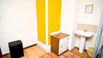 A bathroom with a yellow shower enclosure, a white sink, and a wooden cabinet.