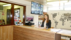 A reception desk with a computer monitor, a keyboard, and a coffee cup. There is a wall with a word cloud and a window in the background. - Kensal Green Backpackers 1 (London)