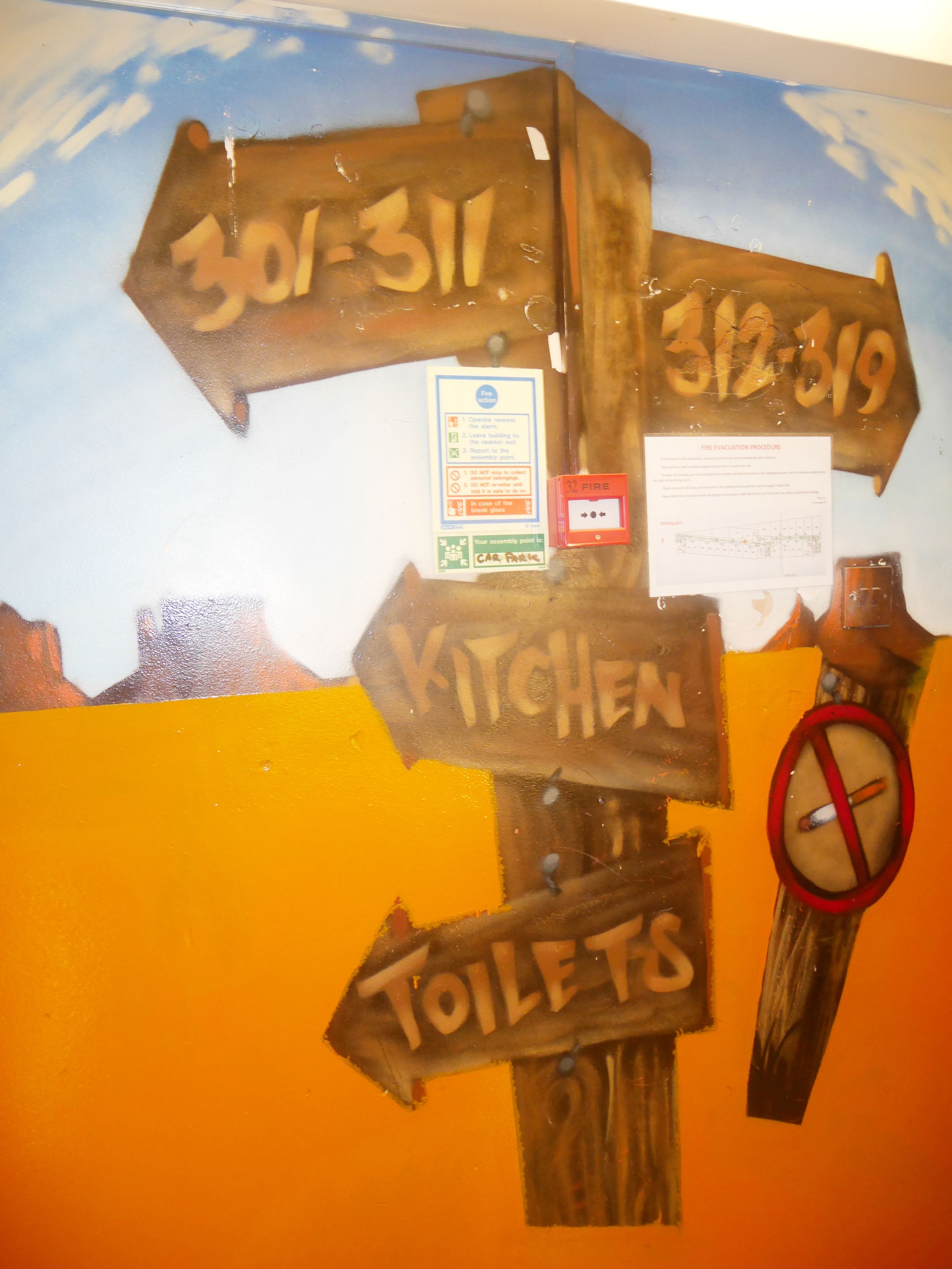 A wall with directional signs pointing to various facilities including a kitchen and toilets.