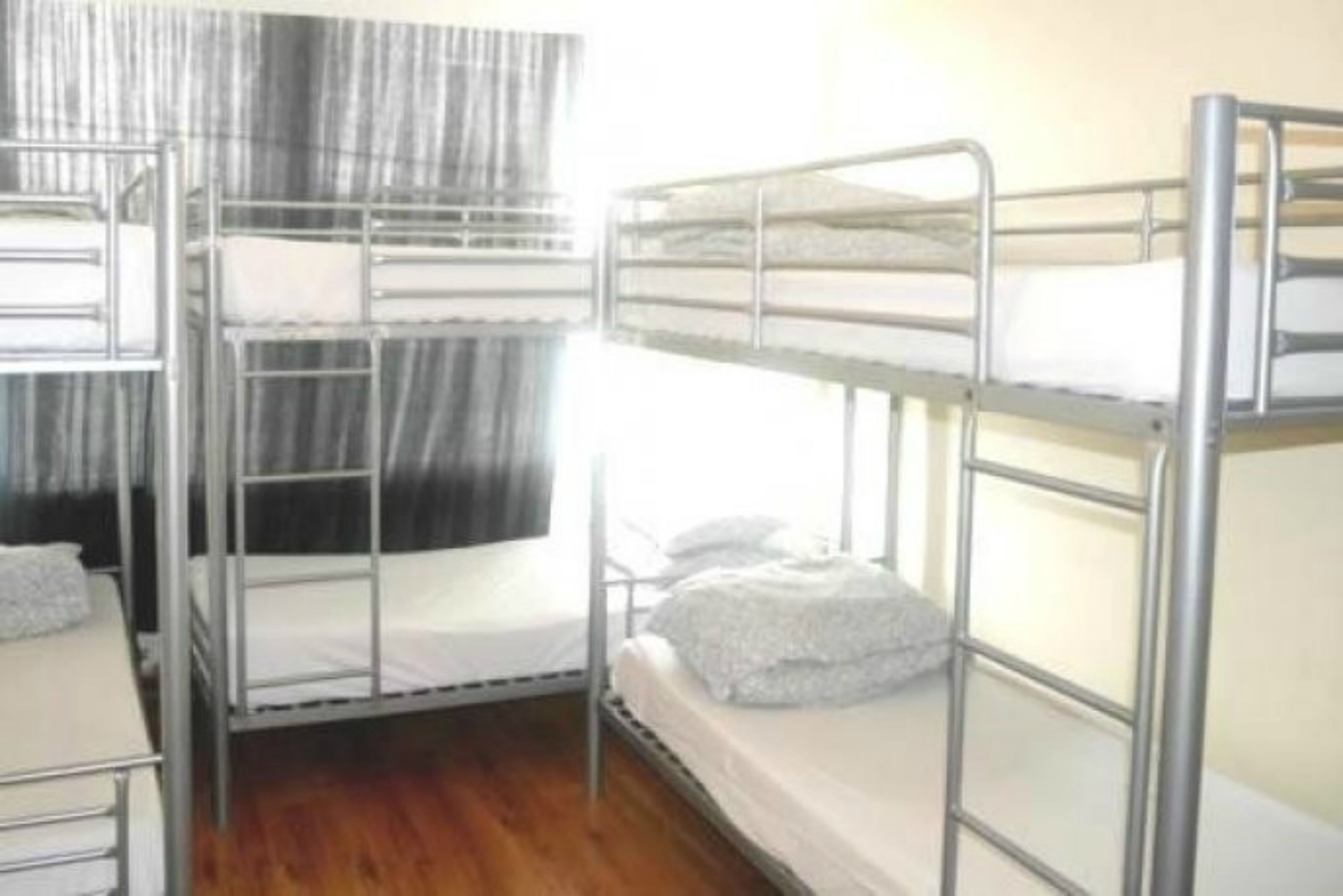 A dormitory room with bunk beds, wooden flooring, and a curtain.