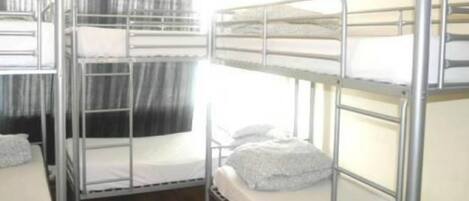 A dormitory room with bunk beds, wooden flooring, and a curtain.