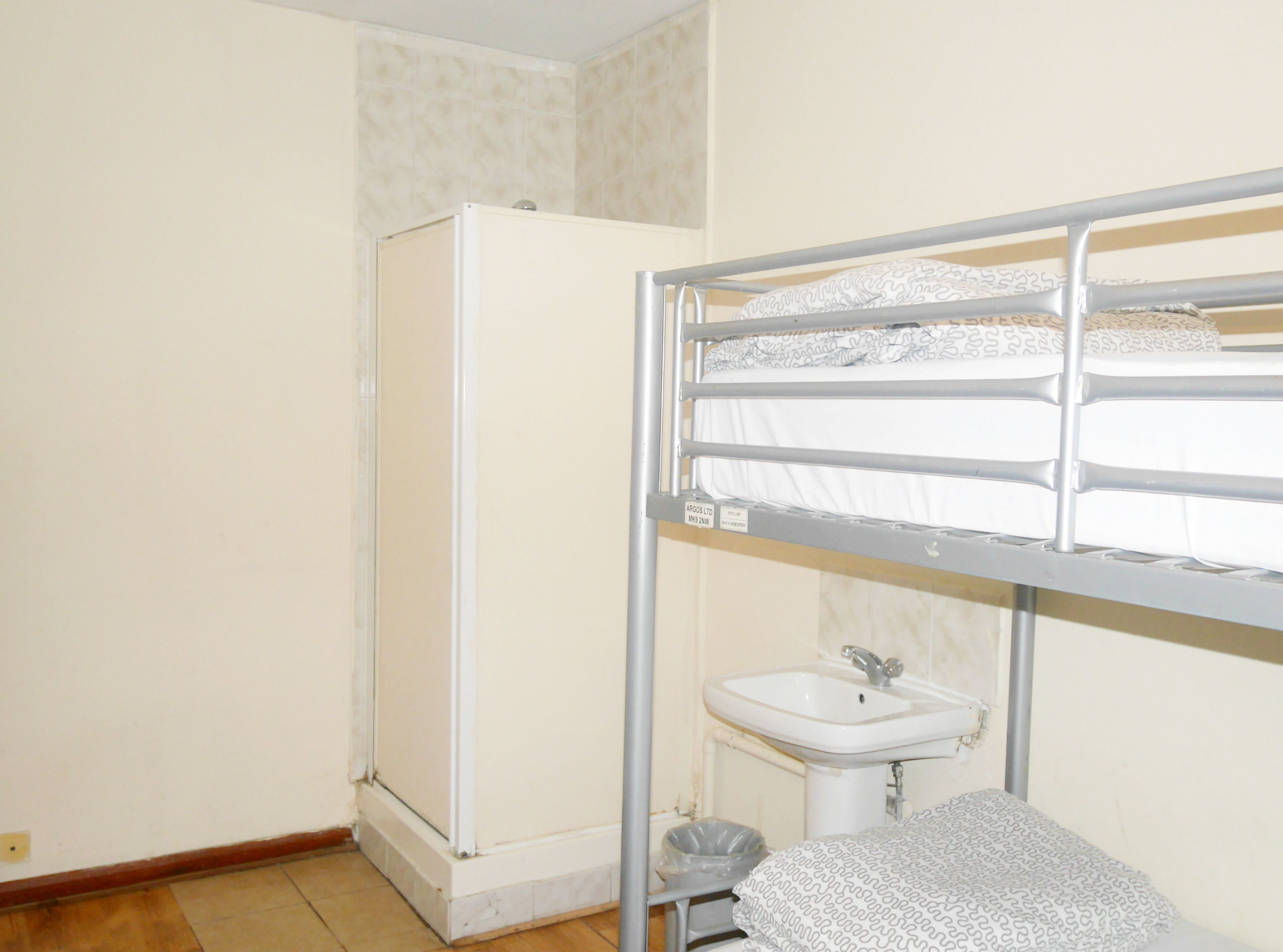 Ein kleiner, kompakter Raum mit Etagenbett, Waschbecken in Weiß und einer kleinen Mülltonne.
