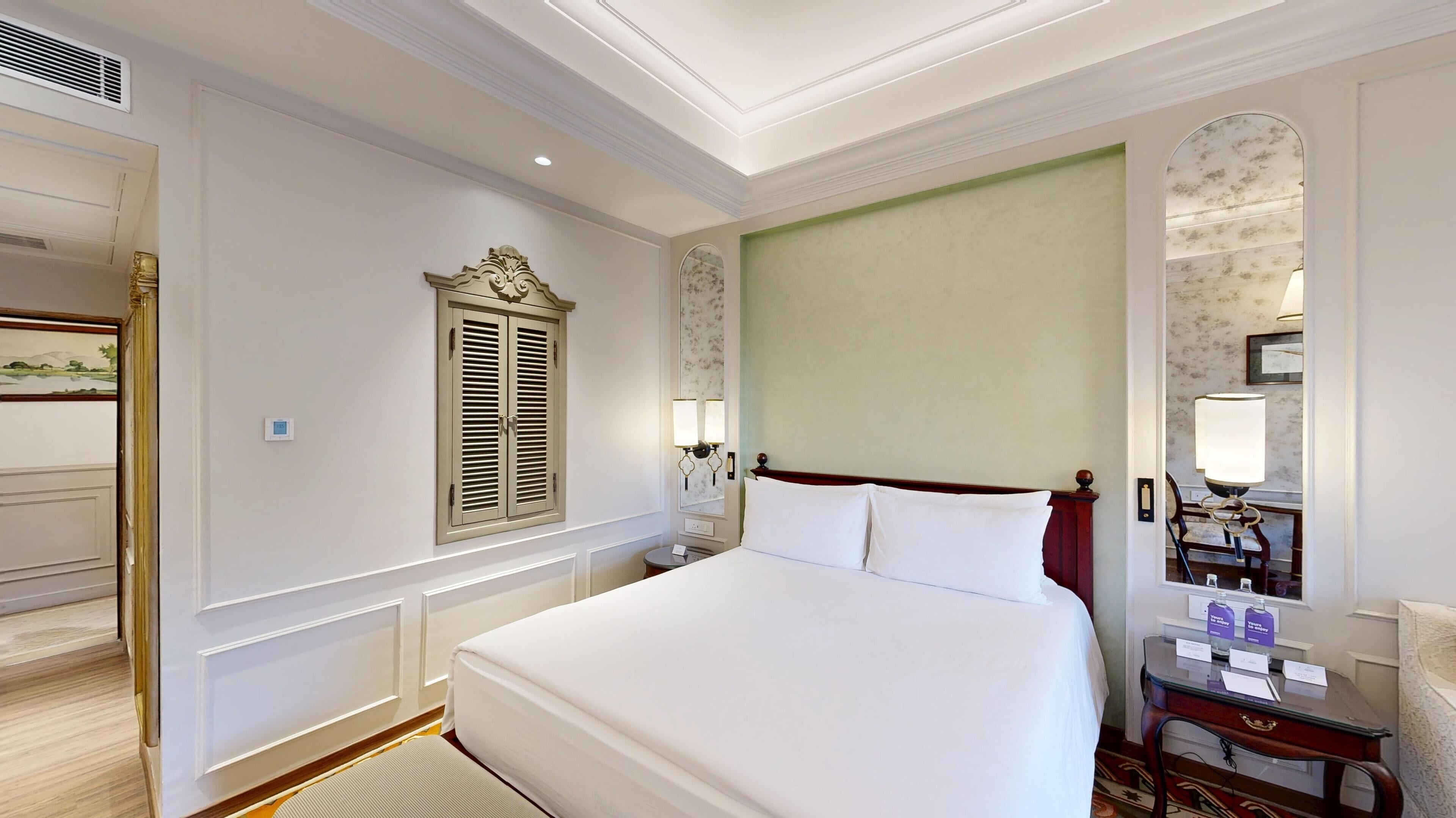 A hotel room with a large bed, a nightstand with a lamp, a mirror, and a door with a view of the outside.