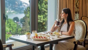 Una mujer sentada a una mesa con una vista panorámica de un lago y montañas a través de amplios ventanales.