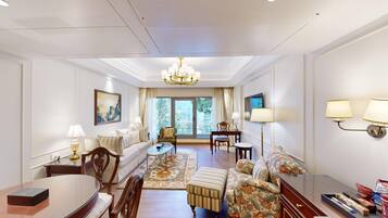 A spacious living room with a sofa, armchairs, a coffee table, and a dining table. There is a chandelier, a television, and a large window with curtains.
