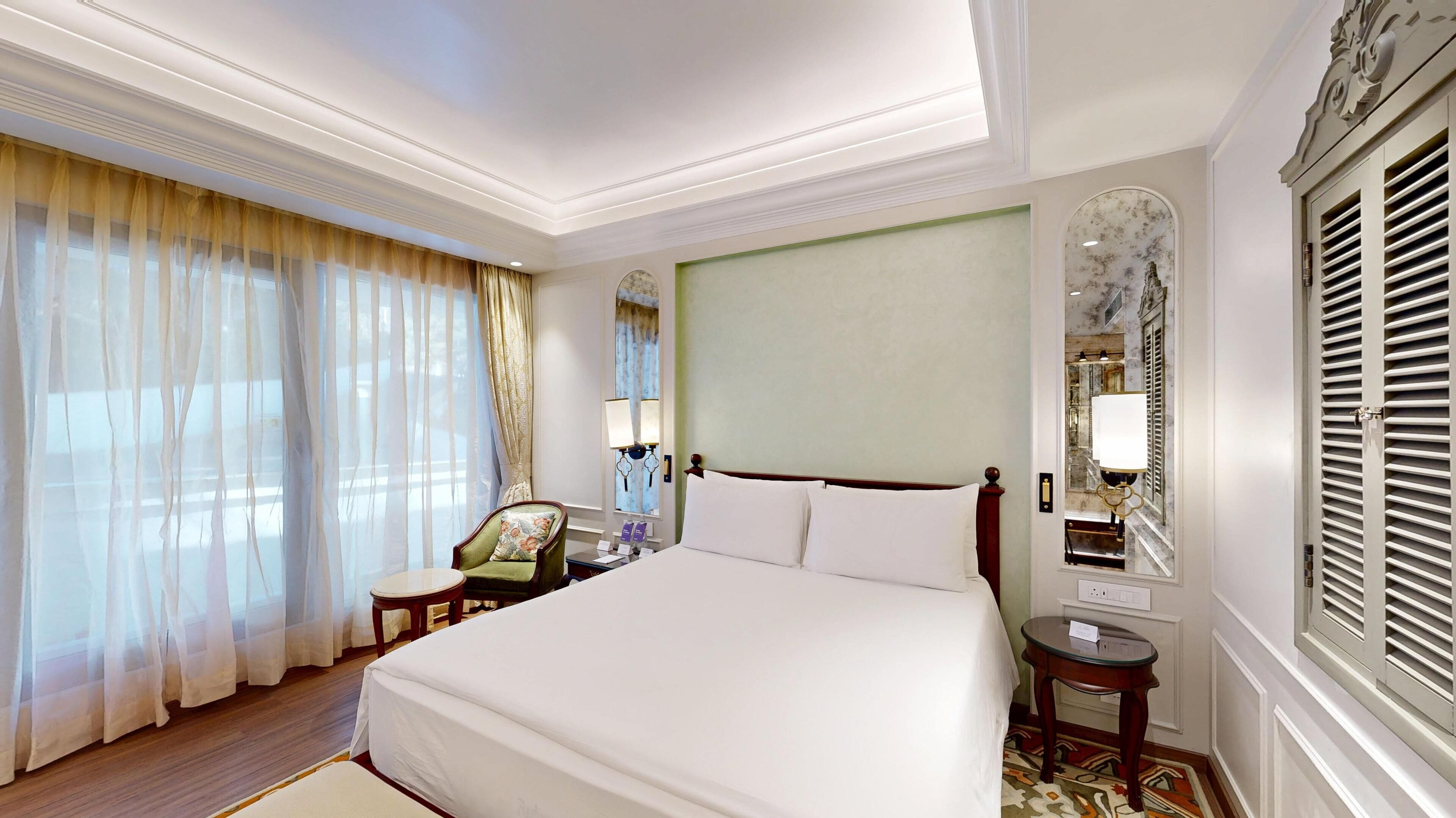 Una habitación de hotel con una cama grande, una silla, una mesita y un espejo.