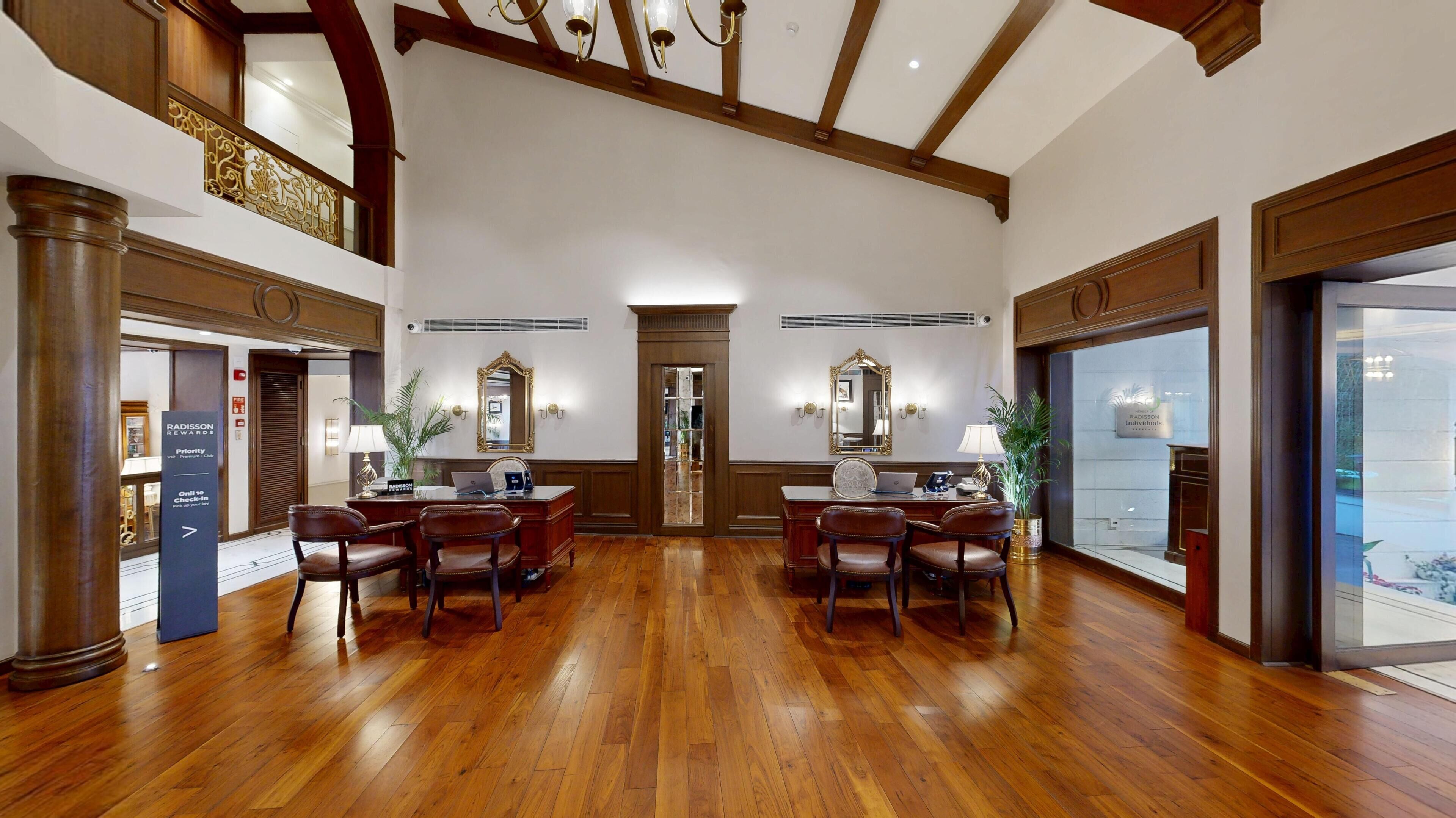 A spacious hotel lobby with wooden flooring, a central reception desk, and a large mirror.
