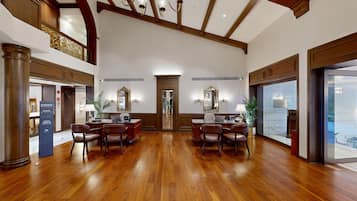 Un amplio vestíbulo de hotel con suelo de madera, un mostrador de recepción central y un espejo grande.