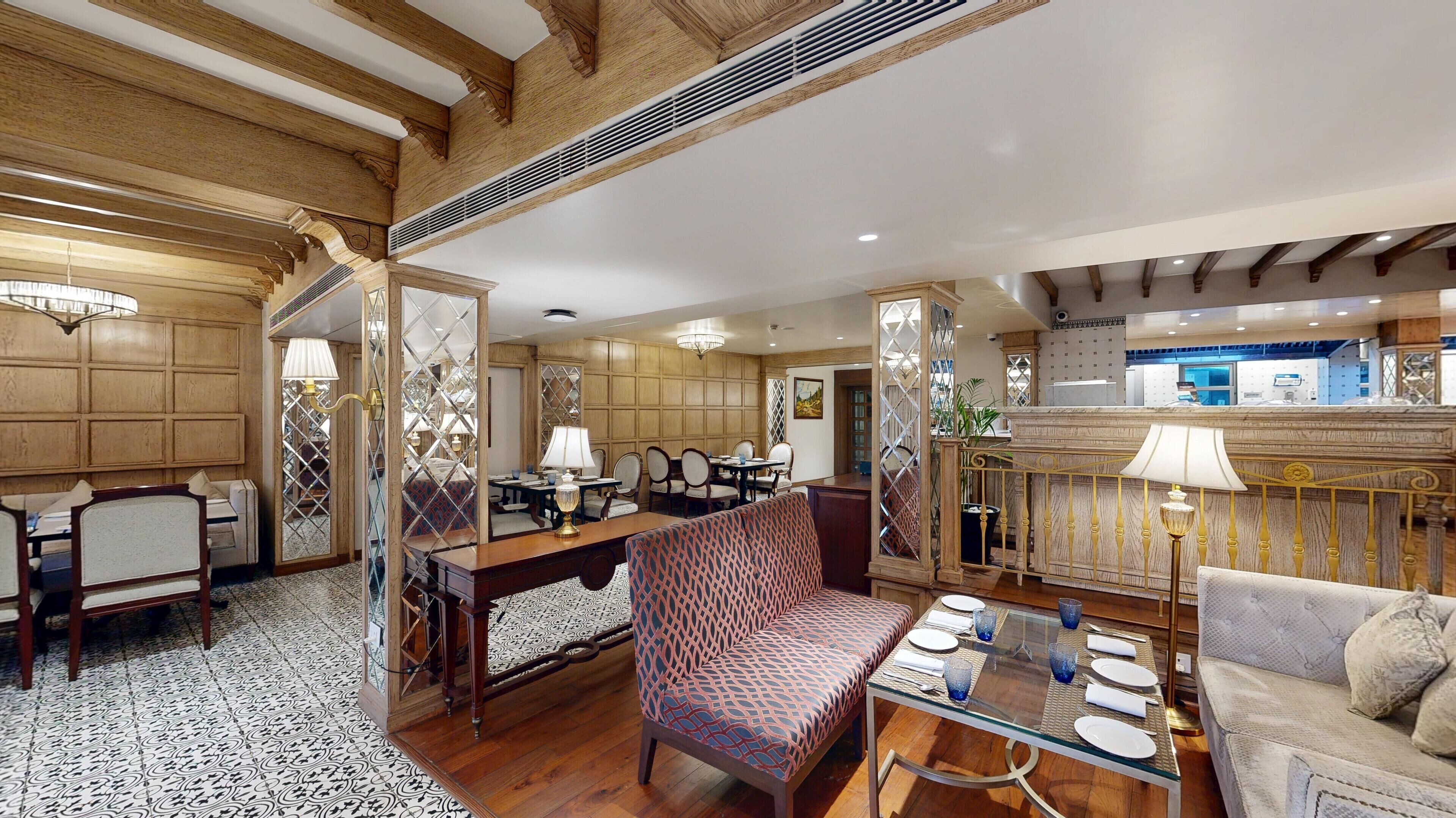 Une chambre d’hôtel spacieuse comprenant un coin repas, un coin salon avec des meubles recouverts d’un tissu à motifs, et une cuisine visible au fond.