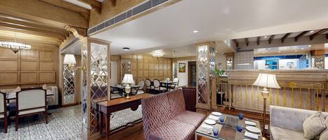 A spacious hotel room with a dining area, a seating area with patterned upholstery, and a kitchen visible in the background.