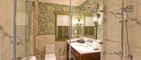 Een badkamer met een douchecabine van glas, een houten wastafelmeubel, een toilet en een spiegel met een bloemistisch behangpatroon.