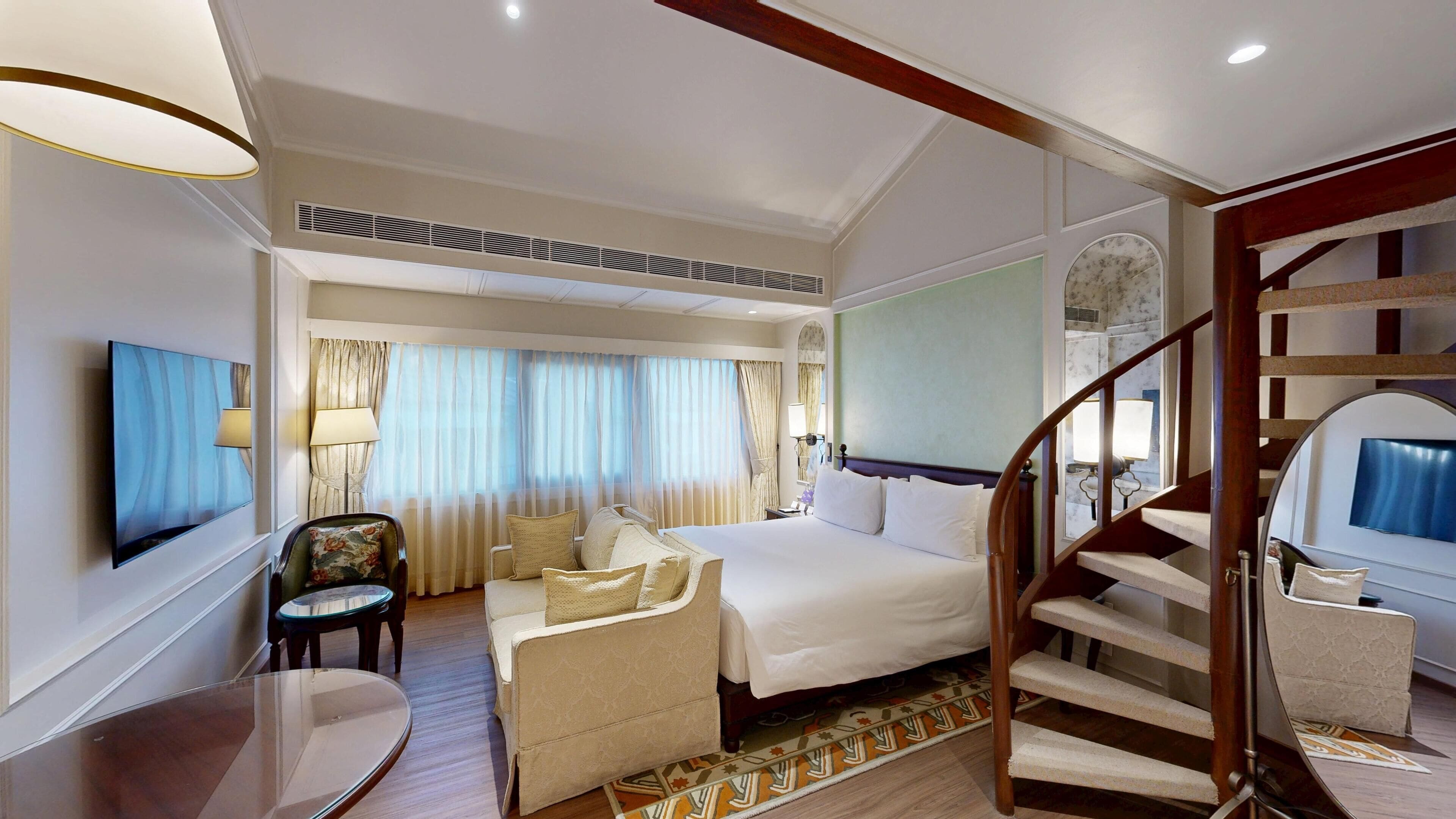 Habitación de hotel con cama, sofá, televisión, escritorio y escalera.