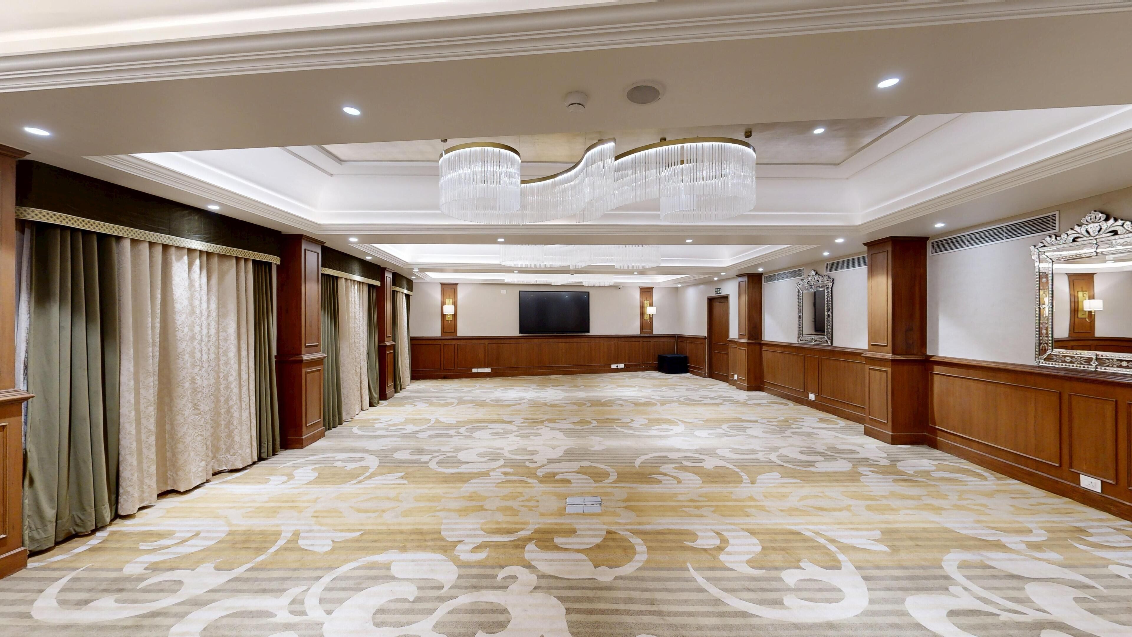 A spacious hotel corridor with a patterned carpet, wooden paneling, and a large chandelier.