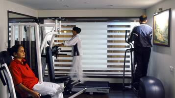 Ein Fitnessraum mit Trainingsgeräten, Laufband und einer Person, die das Laufband benutzt.