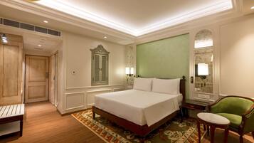 A hotel room with a large bed, a green armchair, a small table, and a wooden bench.