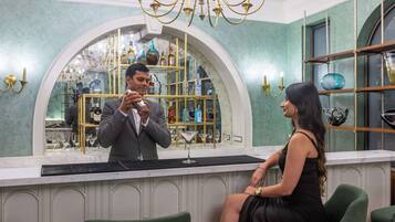 A bar area with a counter, a woman seated, and a man standing behind the counter.