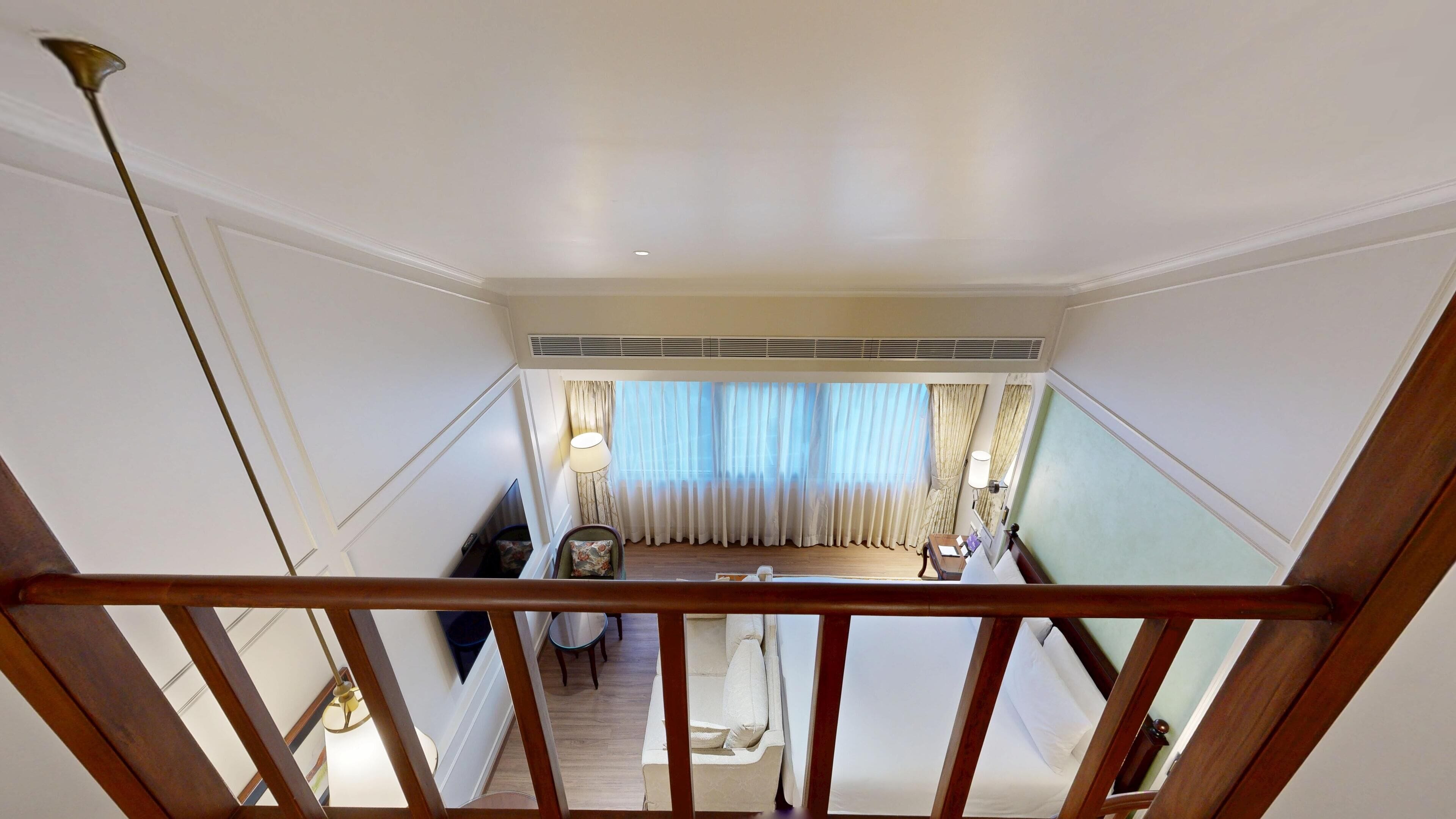 A hotel room with a balcony, a dining area with a table and chairs, and a view of the outside through large windows.