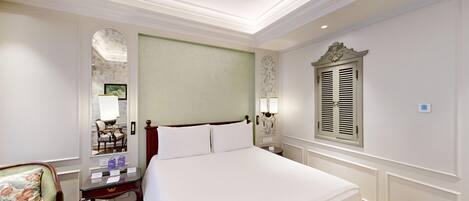 Habitación de hotel ordenada con una cama grande, un escritorio con silla, un espejo y una ventana con contraventanas.