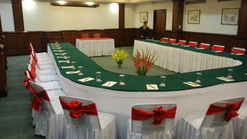 Een congrescentrum met een lange tafel, witte stoelen versierd met rode linten en een groene tafelkleed.