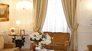 A well-lit living room with a chandelier, a sofa, armchairs, a coffee table, and a vase of flowers. - Villa Pinciana (Rome)