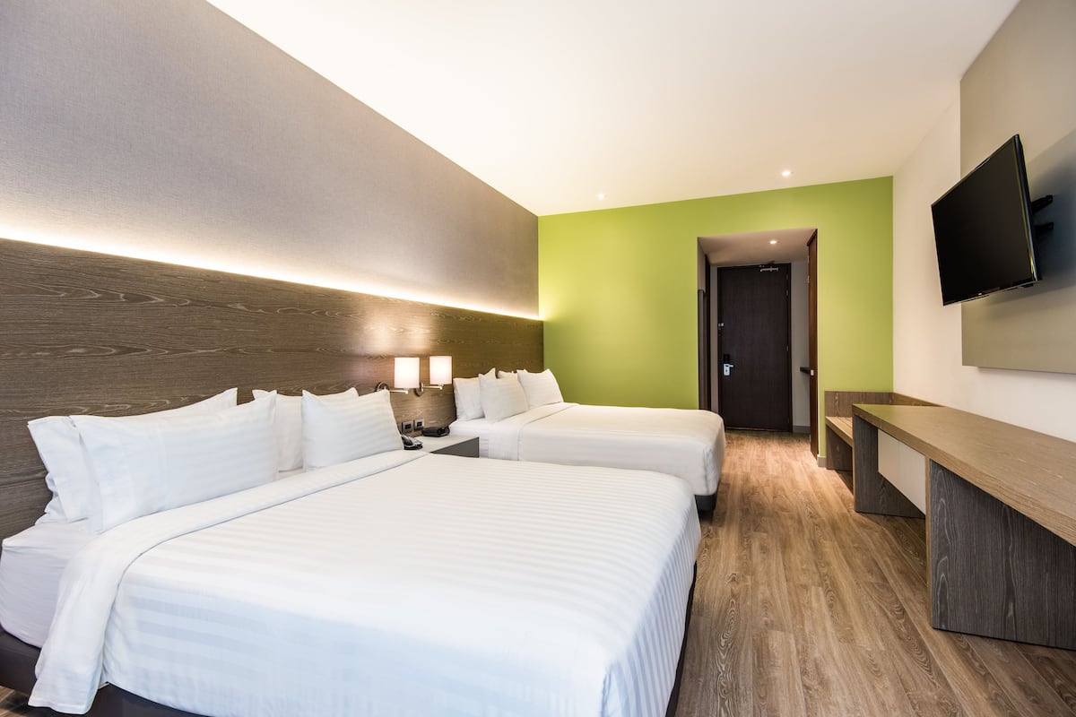Habitación de hotel con dos camas, un escritorio, un televisor y una pared de acento verde.