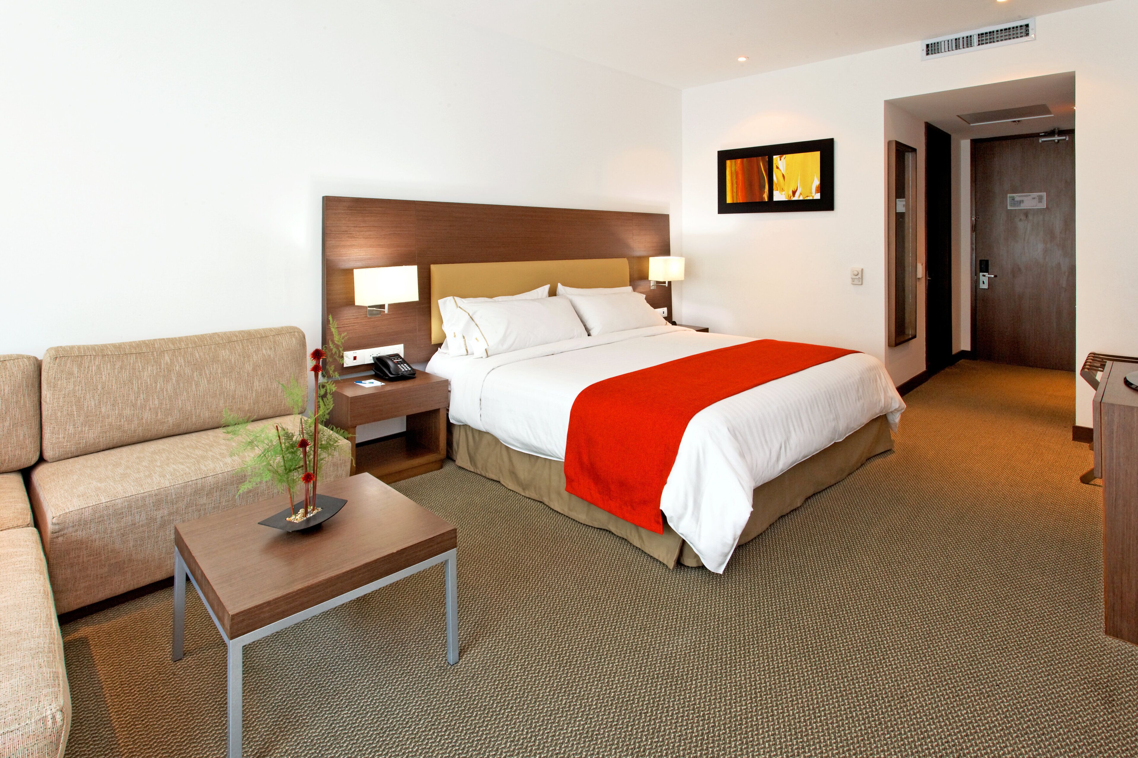 Habitación de hotel con cama, mesita de noche, escritorio, silla y puerta.