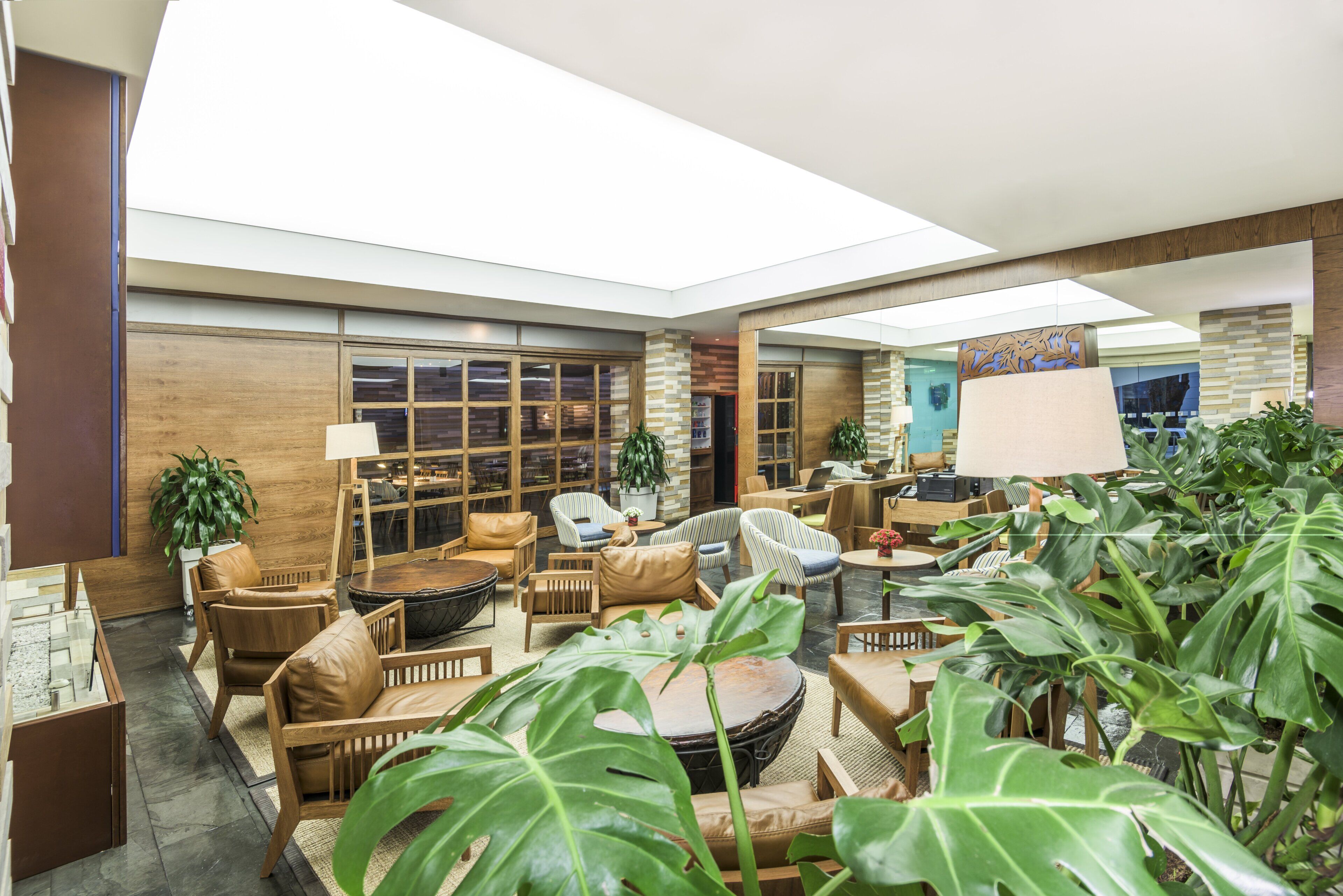 A spacious indoor area with multiple seating arrangements, including sofas and chairs, surrounded by large potted plants.