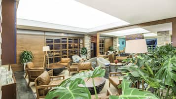 A spacious indoor area with multiple seating arrangements, including sofas and chairs, surrounded by large potted plants.
