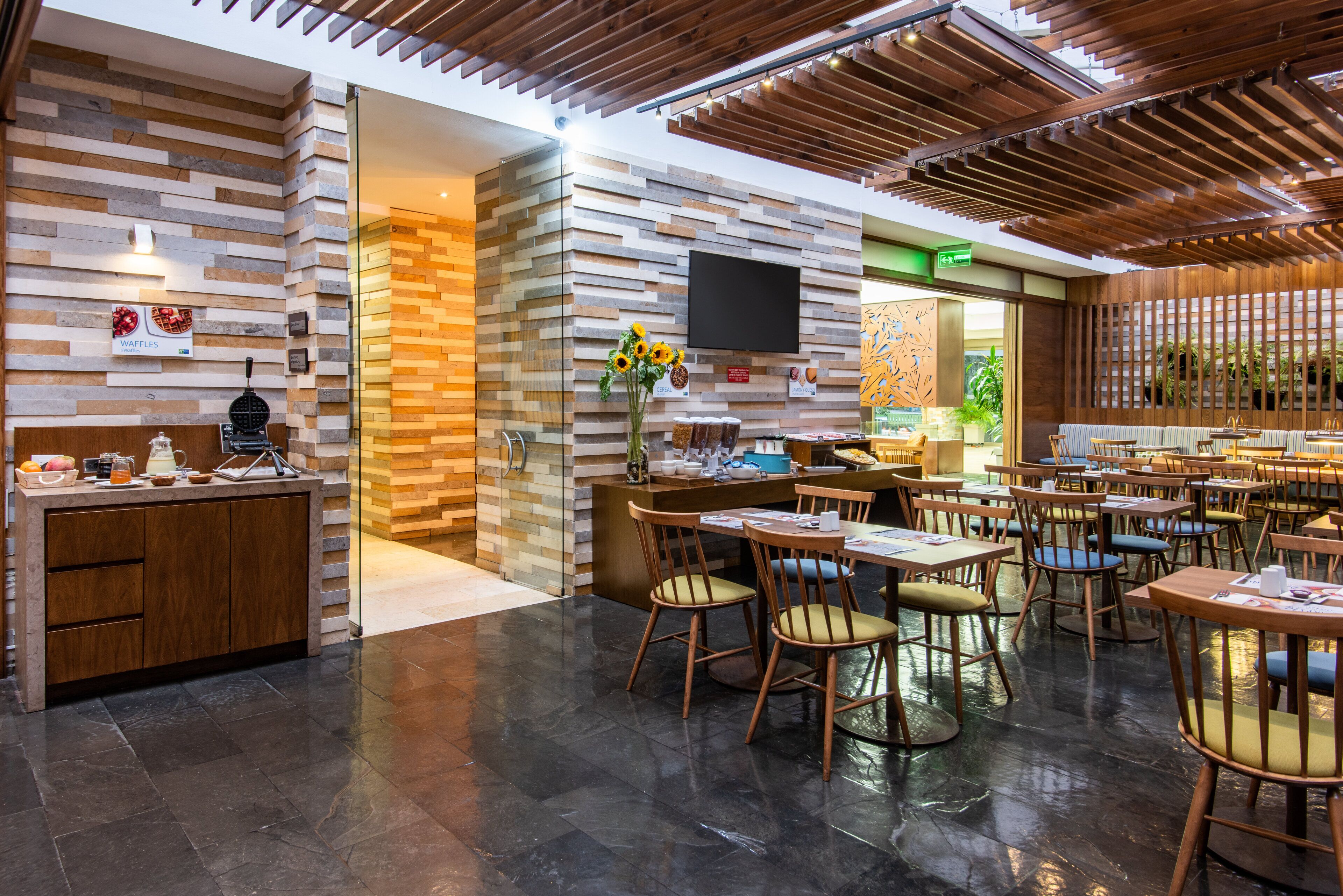 Een modern restaurantinterieur met een bakstenen muur, houten plafond en diverse zithoekopstellingen.