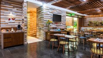 Een modern restaurantinterieur met een bakstenen muur, houten plafond en diverse zithoekopstellingen.