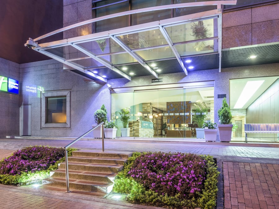 Fachada de hotel de vidrio, con asientos al aire libre y una escalera que conduce a la entrada.