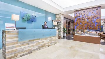 A hotel reception desk with a modern design, a receptionist, and a decorative wall with leaf patterns.