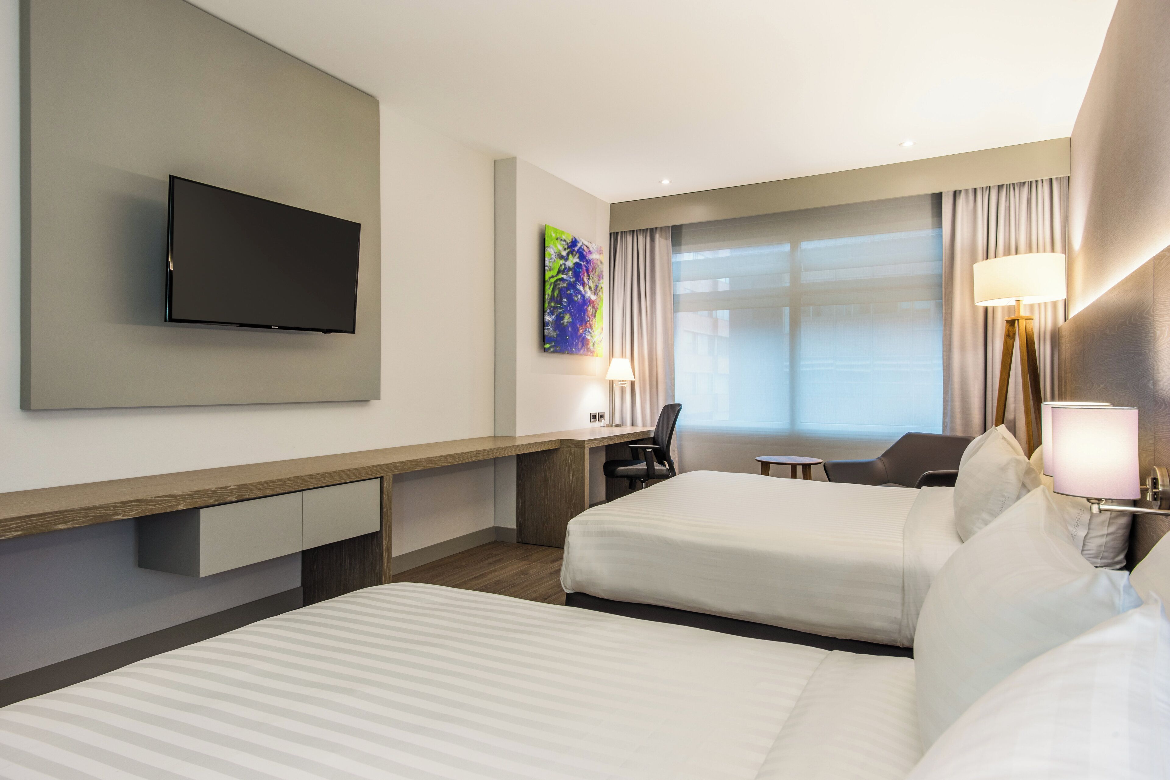 A hotel room with two beds, a desk, a chair, a television, and a window with curtains.