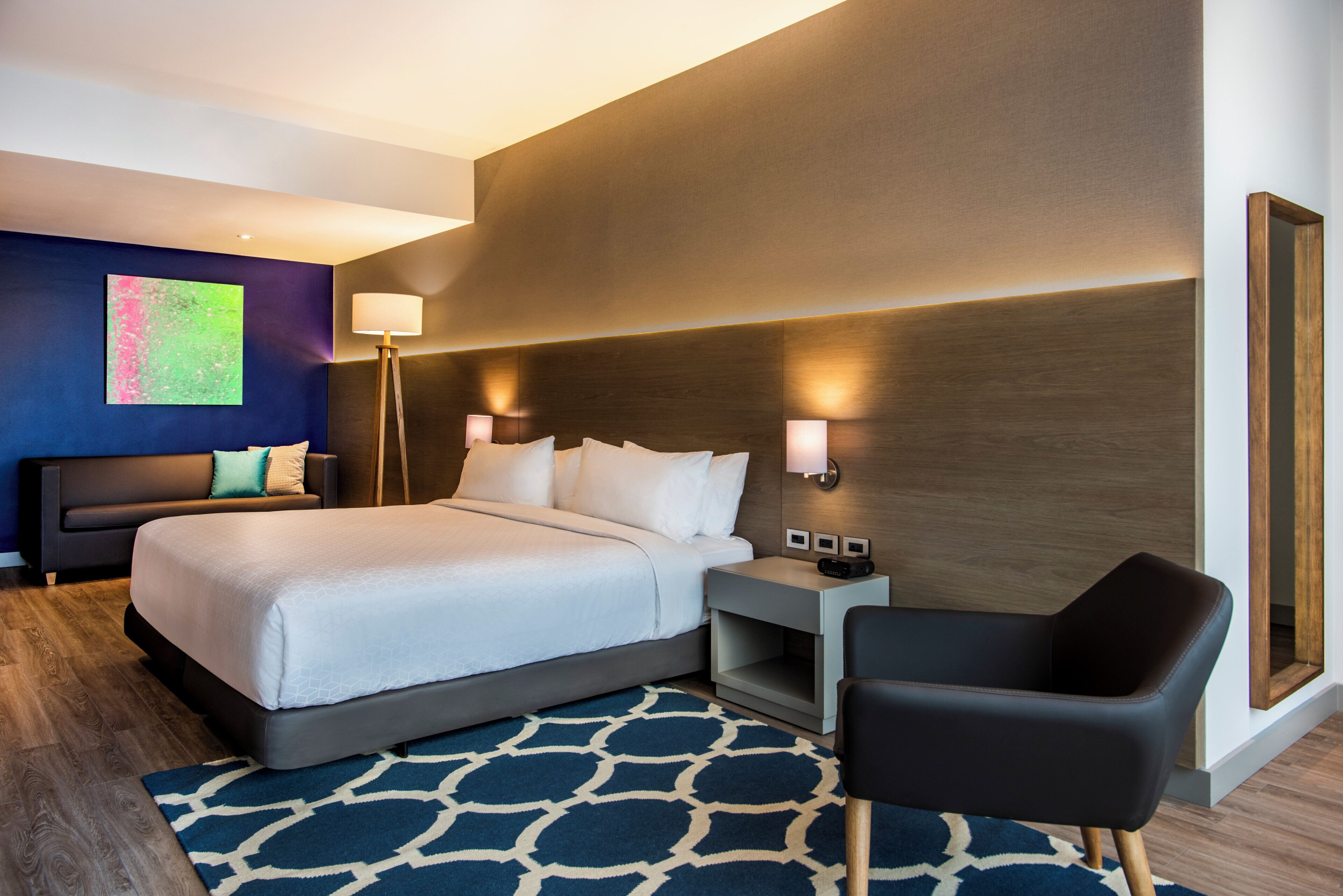 Ett modernt hotellrum med en stor säng, sängbord, en stol och en stor spegel.