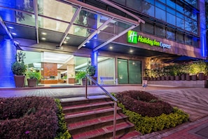 Edificio de Holiday Inn Express con fachada moderna, zona de estar al aire libre y una escalera que lleva a la entrada.