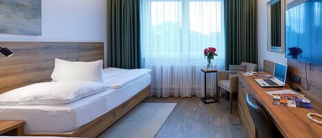 Una camera d'albergo con un letto, una scrivania con un portatile, una sedia e una finestra con tende.