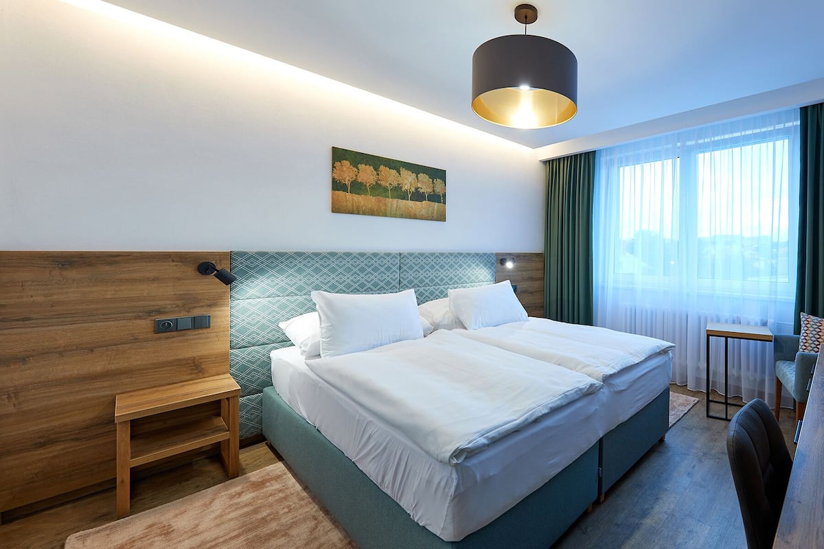 Een hotelkamer met een groot bed, een houten bankje, een schilderij en een raam met gordijnen.