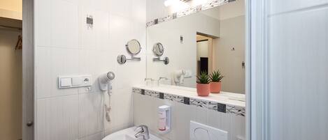 A modern bathroom with a white sink, two mirrors, a hairdryer, and a potted plant on the vanity.