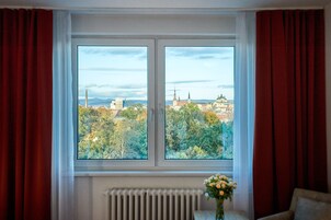 Una habitación con una ventana grande, cortinas rojas, un radiador y un florero con flores.