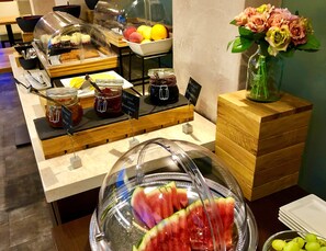 Un bufé con diversos alimentos, incluyendo una exhibición de sandía y un tazón de uvas.