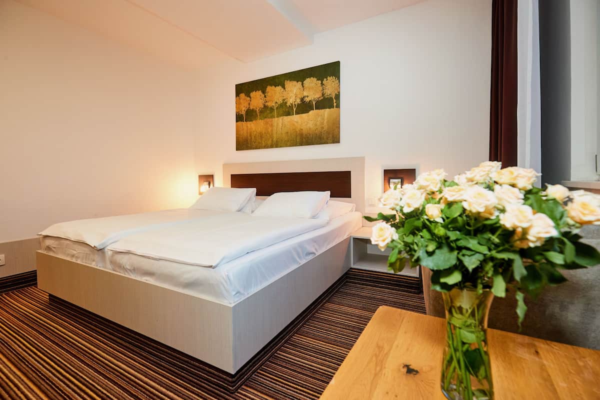 Een hotelkamer met een groot bed, nachtkastjes, een schilderij aan de muur en een bloevas op een houten tafel.