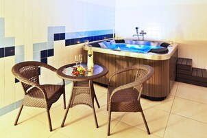 A hot tub with a table and two wicker chairs in a tiled room.