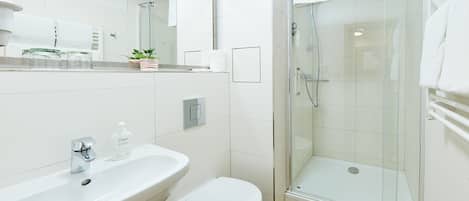 Un baño moderno con cabina de ducha de vidrio, un lavamanos blanco y un inodoro.