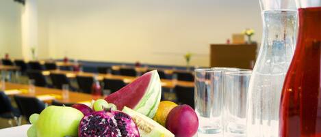 Una bandeja de frutas sobre una mesa, con vasos de agua y una botella de bebida roja.